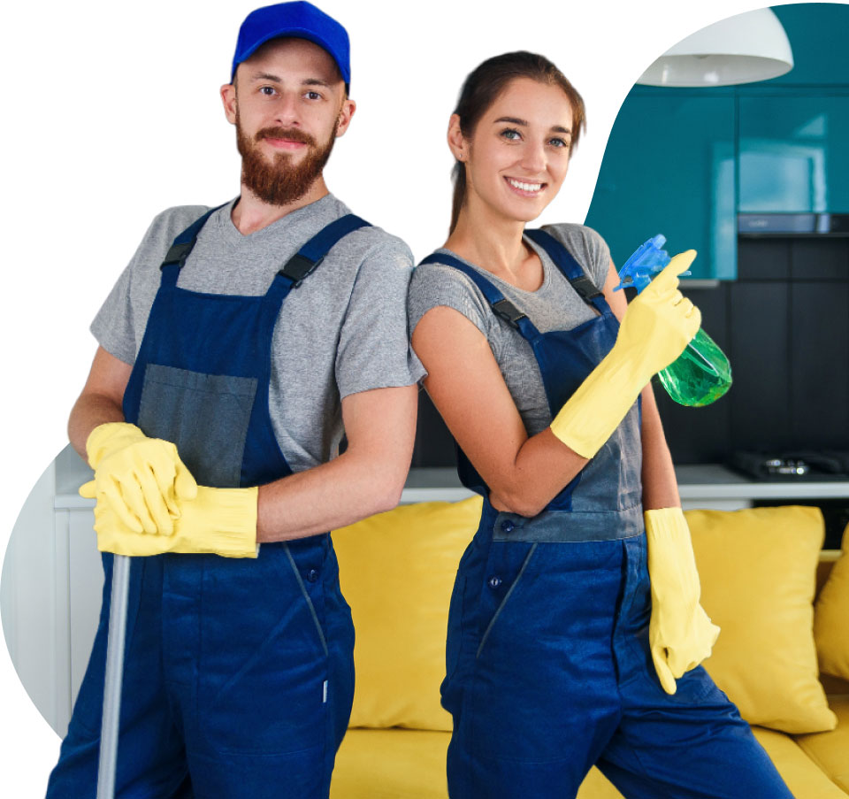 Two smiling cleaners in blue overalls and yellow gloves stand back-to-back with cleaning supplies in hand, in a bright, modern kitchen setting.