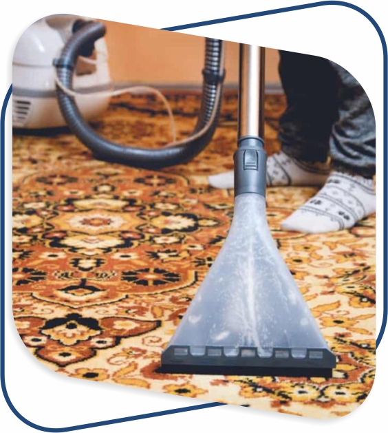 A person in patterned socks uses a vacuum cleaner on an ornate, colorful carpet. The focus is on the vacuum's nozzle and the intricate carpet design.